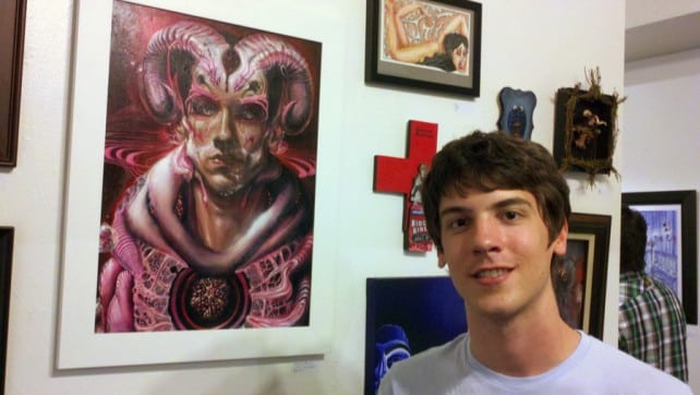 Aaron Bolton smiling with his painting, "The Scapegoat", at Hive Gallery